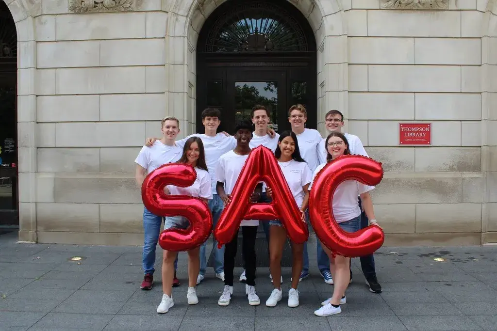 SAC group photo of students wearing white shirts and holding scarlet letter balloons that say SAC