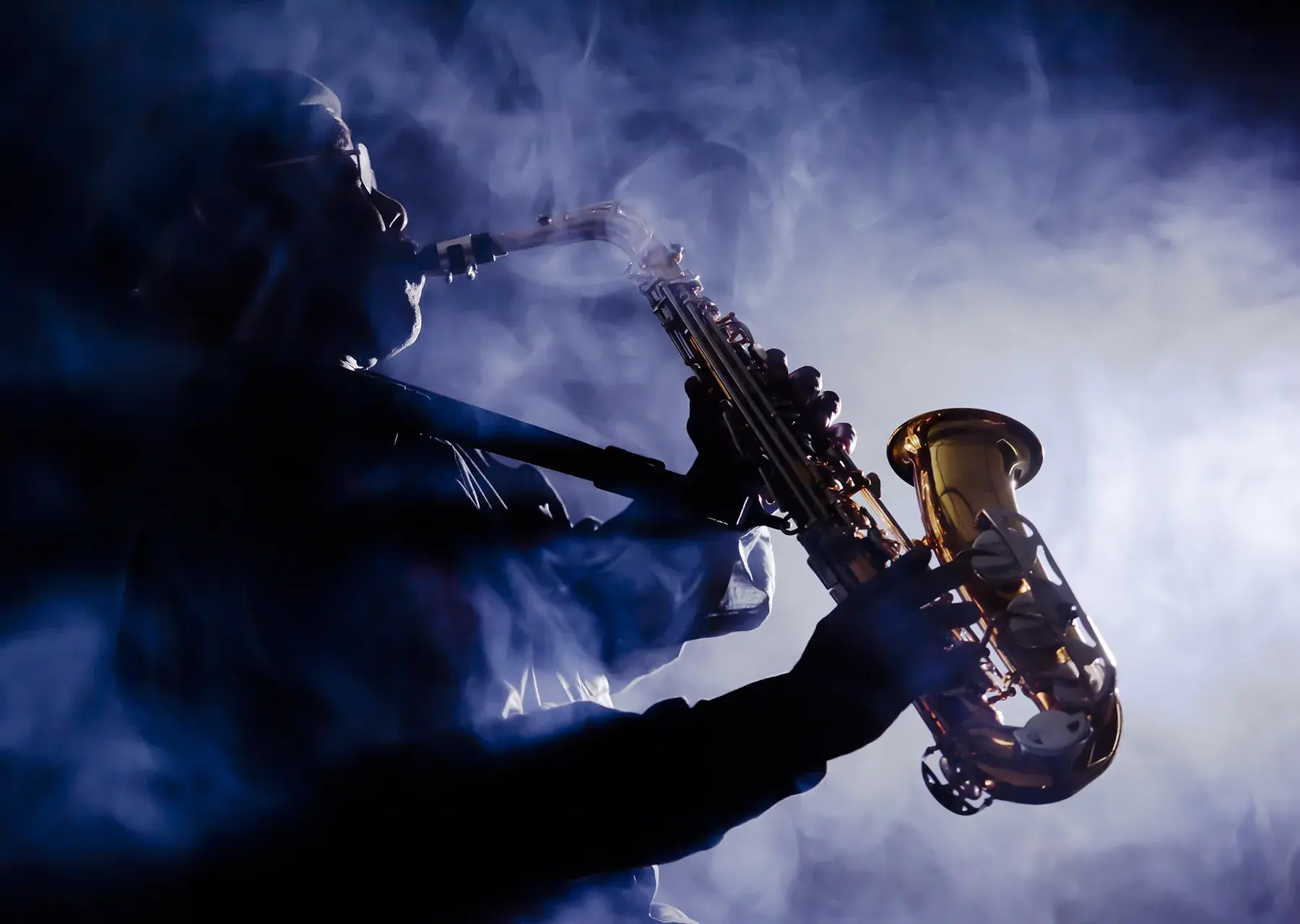 A person playing a saxophone with a spotlight and smoke in the background