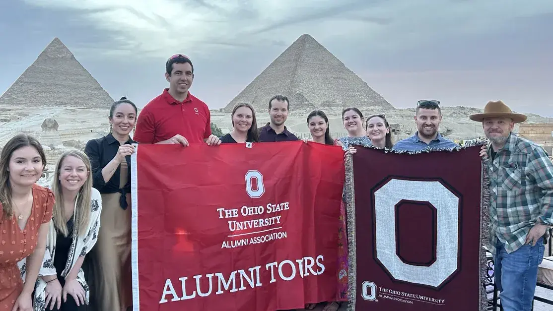 dozen people pose with an ohio state flag in front of the Great Pyramids