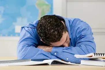 man in blue button up, with his head down on his textbooks