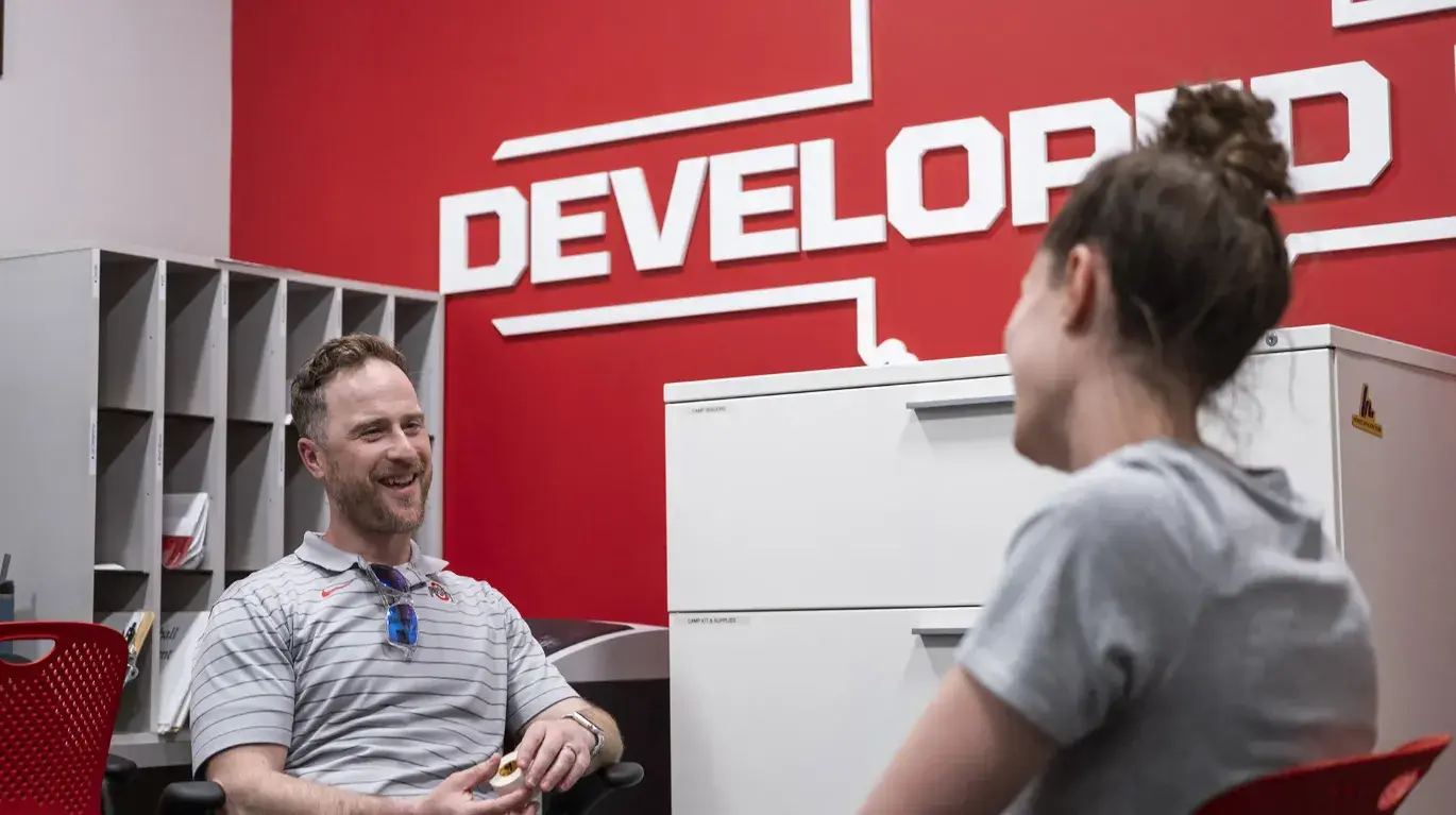 Two athletic trainers talk in an office with Developed on the wall in the background
