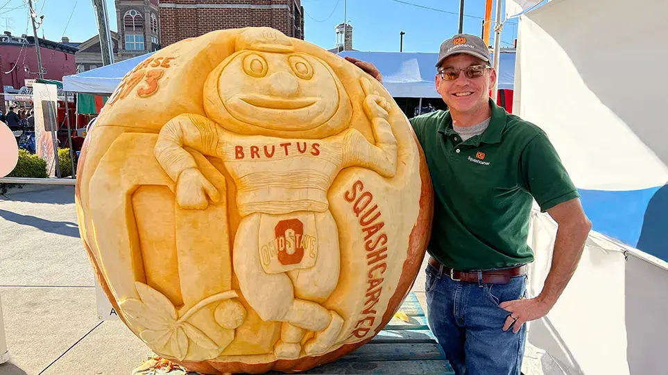 Gus Smithhisler grins as he shows off a giant pumpkin he just carved. It has Brutus Buckeye leaning on a Block O.