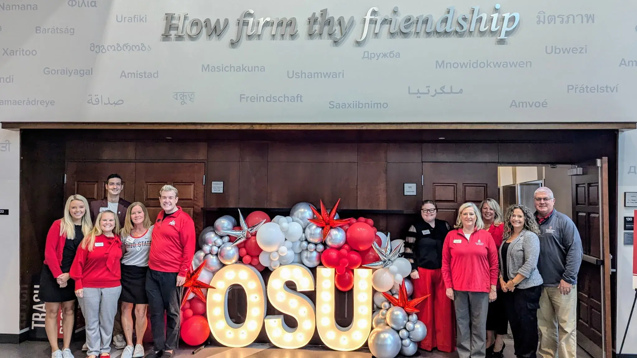 team standing around OSU sign and scarlet and gray balloons smiling