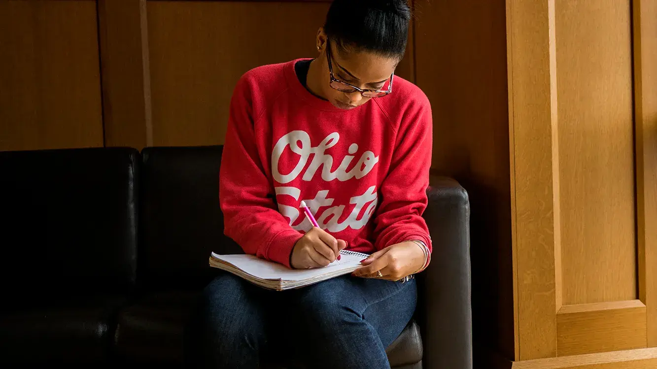 woman wearing a scarlet sweater writing on a notepad