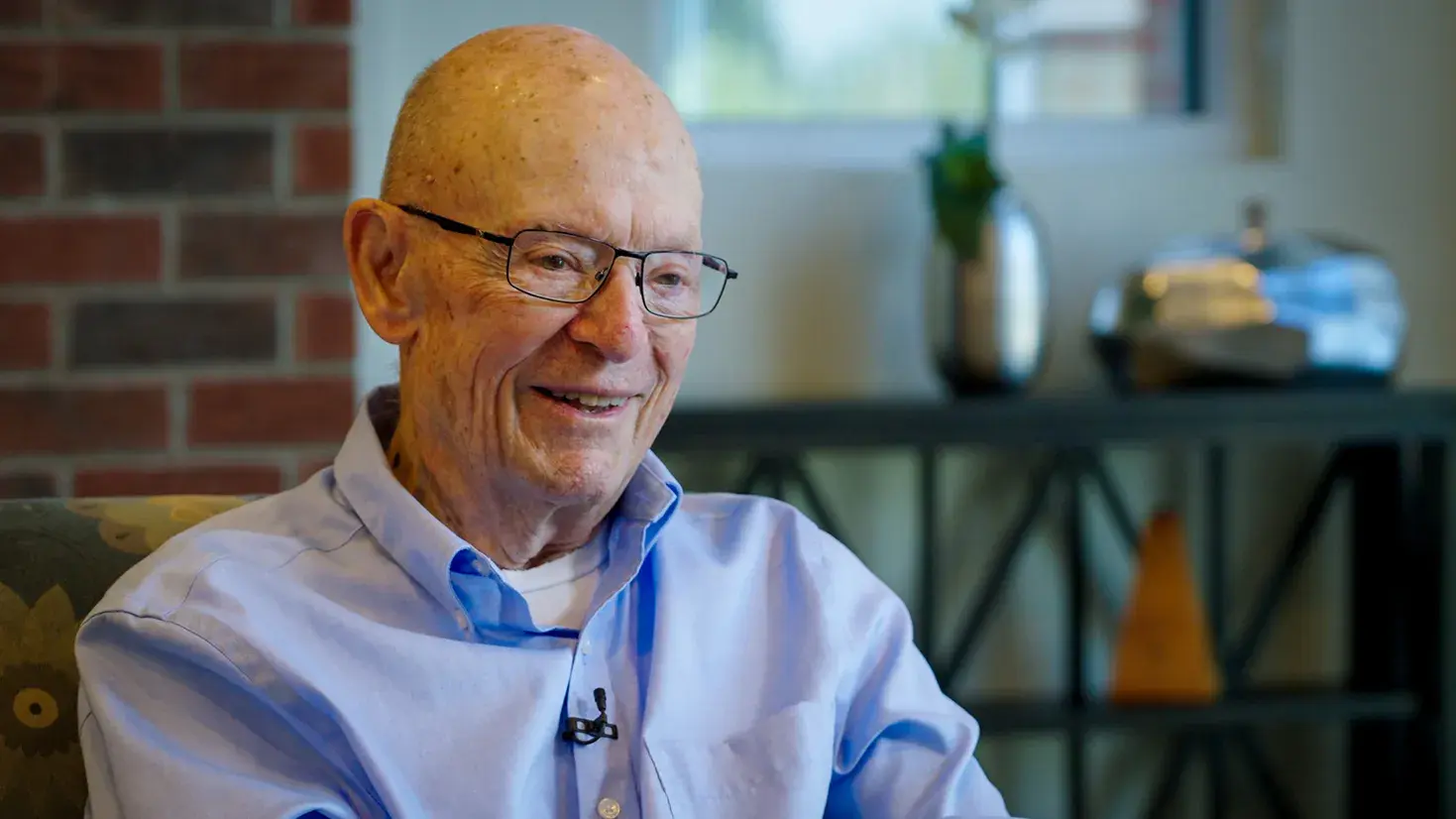 Dick Wood smiles as he tells a story. He's an older white man wearing glasses and a button-up shirt. Lines on his face shows he's smiled a lot through his years.
