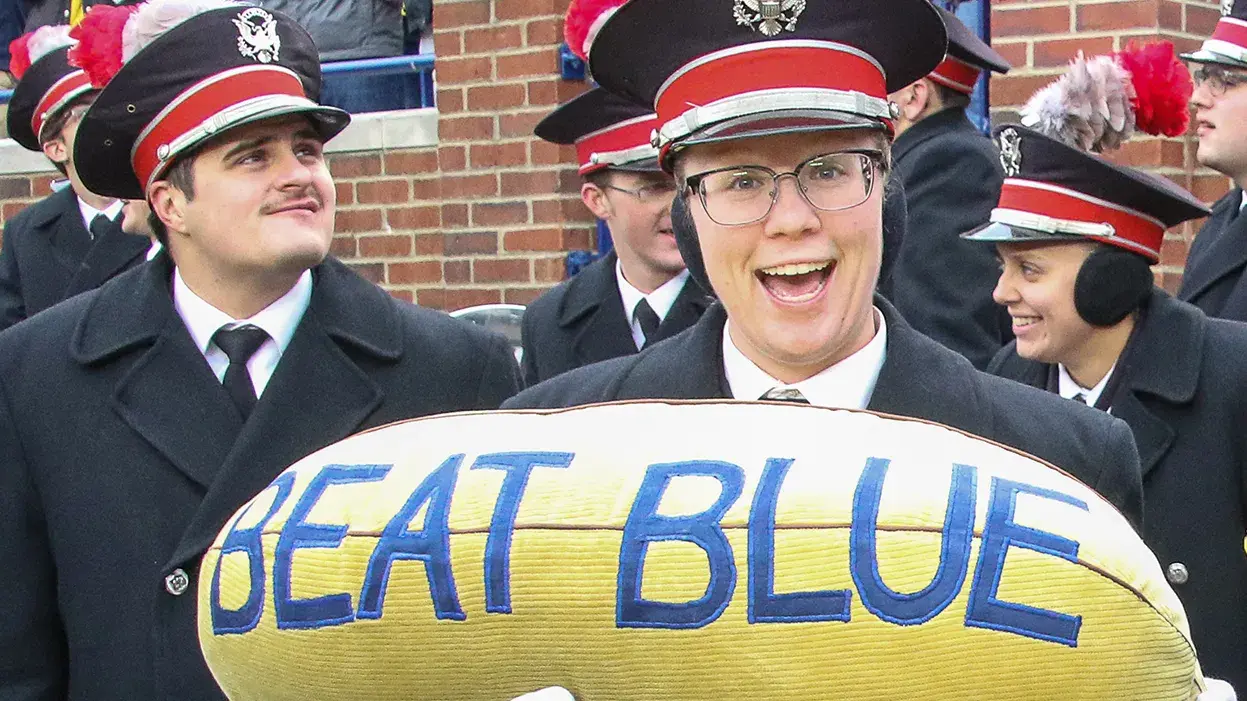 ohio state marching band member holding a yellow banana plush with the words "beat blue"