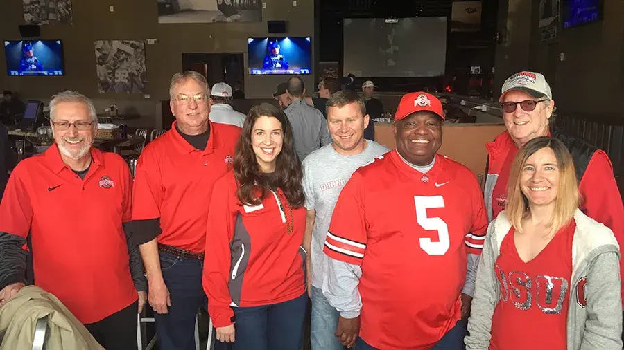 Group of individuals in their Ohio State clothes standing together for photo in a restaurant.