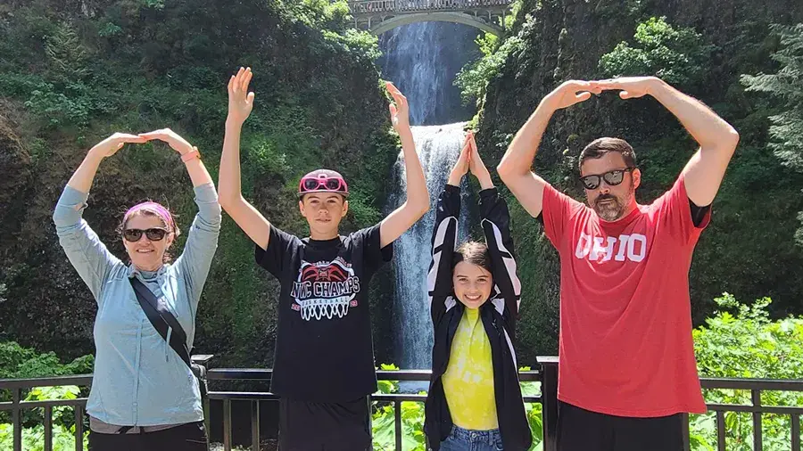 Family of four doing O-H-I-O with their arms in front of a waterfall.