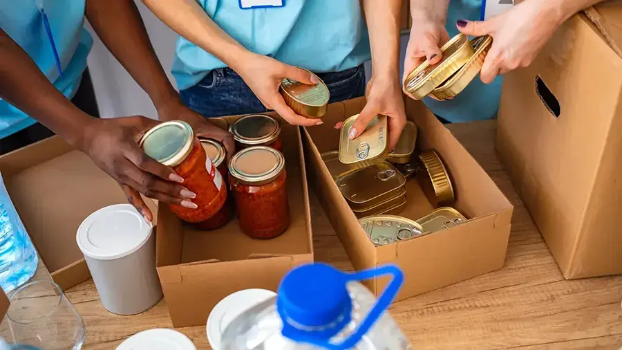 Various hands putting food items in boxes.