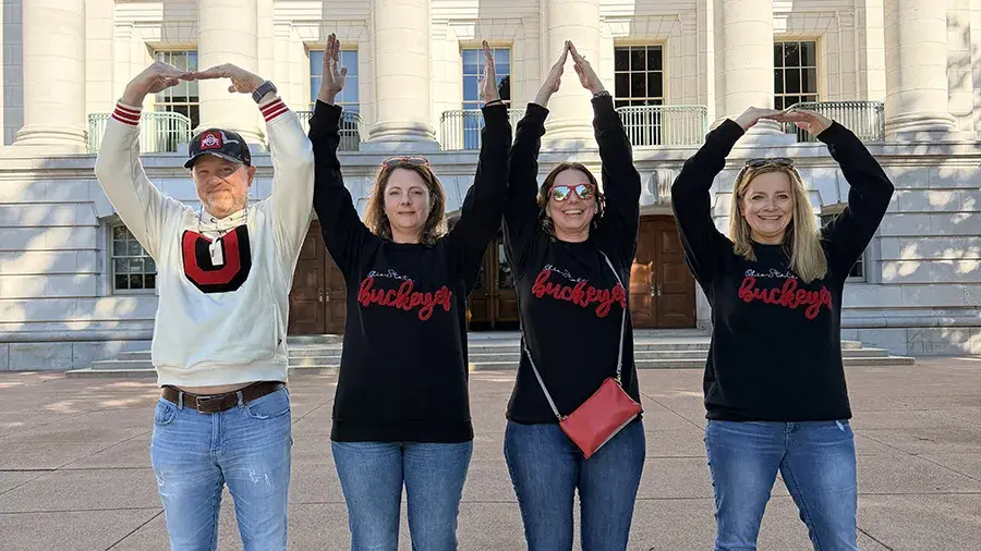 4 individuals doing O-H-I-O with their arms in front of a building in Wisconsin.