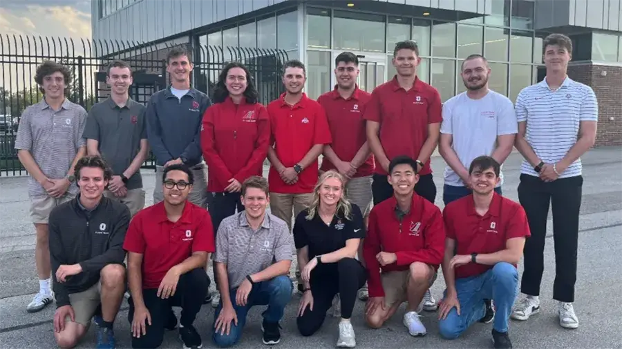 Group of individuals in their red and gray attire posing in front of an aviation building outside.