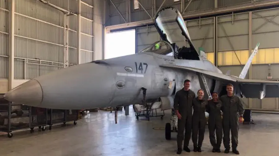 Naval members standing indoors next to a plane.