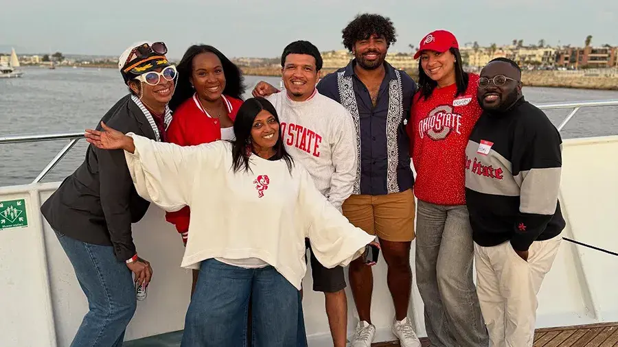 Group of individuals standing on a boat in their Ohio State gear posing for a photo.