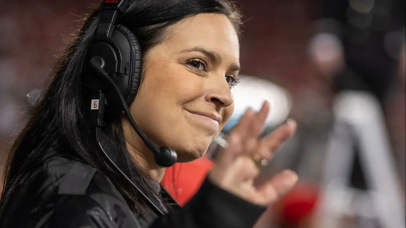 A woman smiles as she waves to someone off camera in this closeup photo of her. She wears a headset to talk to other coordinators.