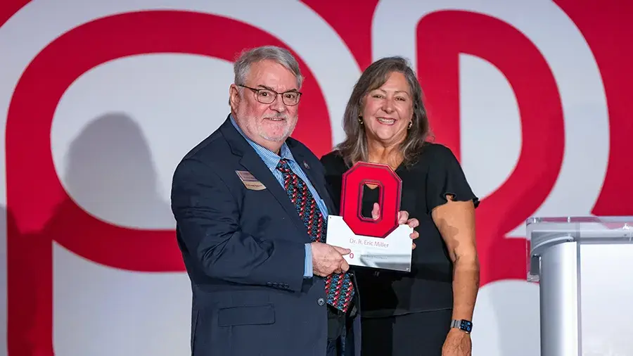 Two individuals standing next to a podium holding a red Block O awards posing for a photo.