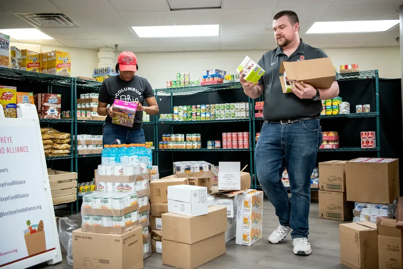 Two individuals moving food items in a food pantry.