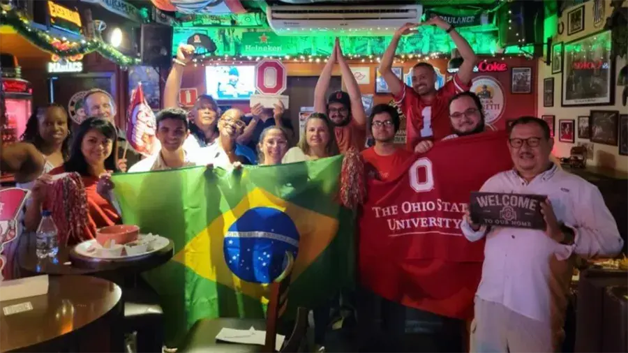 Ohio State alumni standing together in a restaurant holding the national flag of Brazil.
