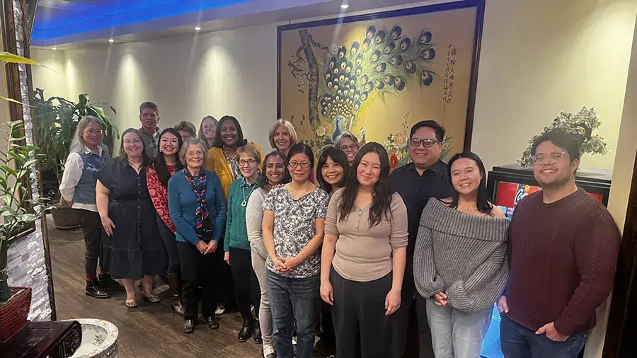 A group of people standing together in a restaurant, posing for a group photo in front of a decorative wall with a large artwork.
