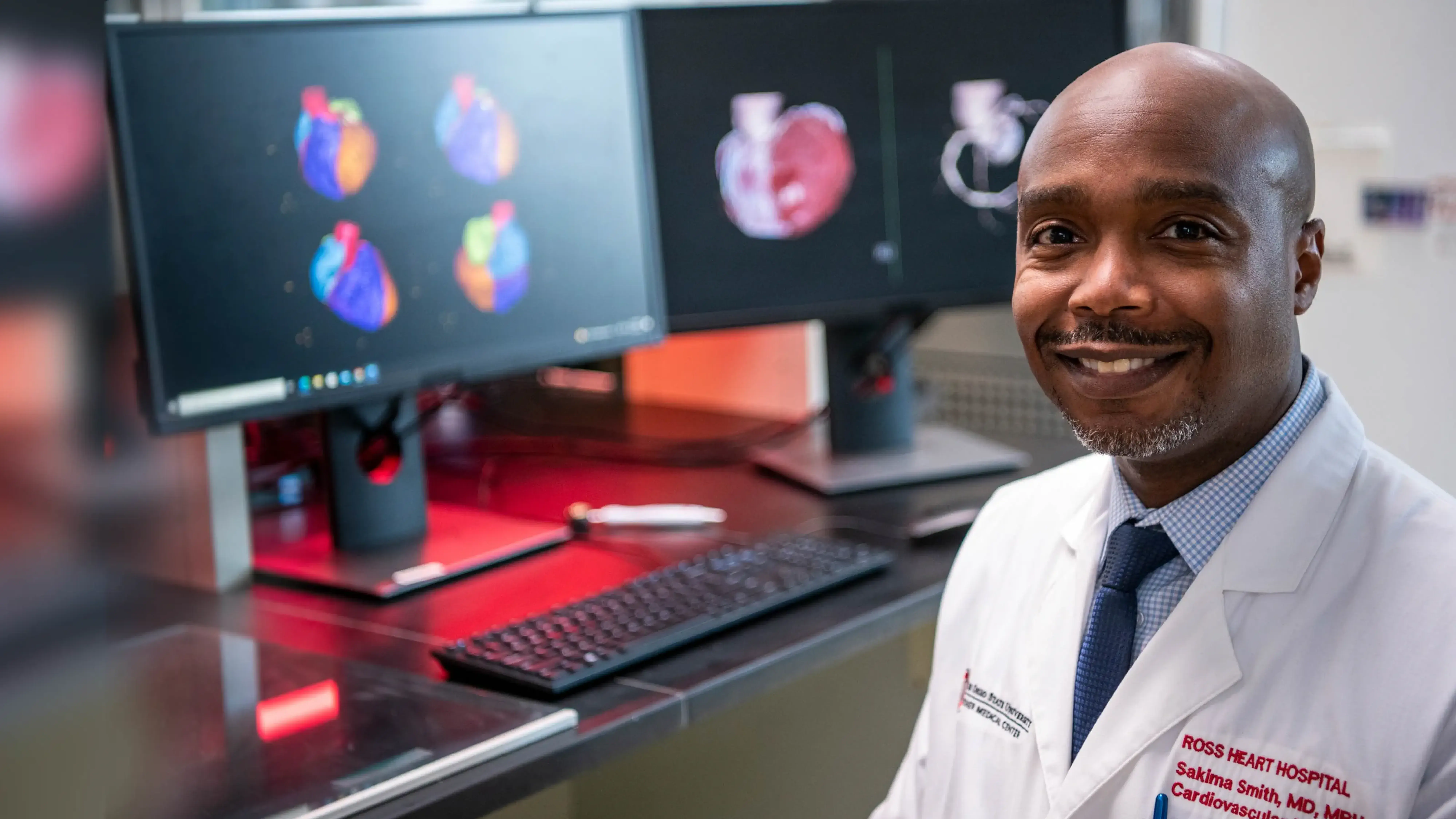 Doctor sitting by a computer with a heart image on the screen.
