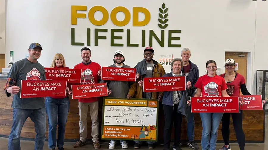 Group of Buckeyes volunteering at Food Lifeline holding Buckeyes Make an Impact signs.