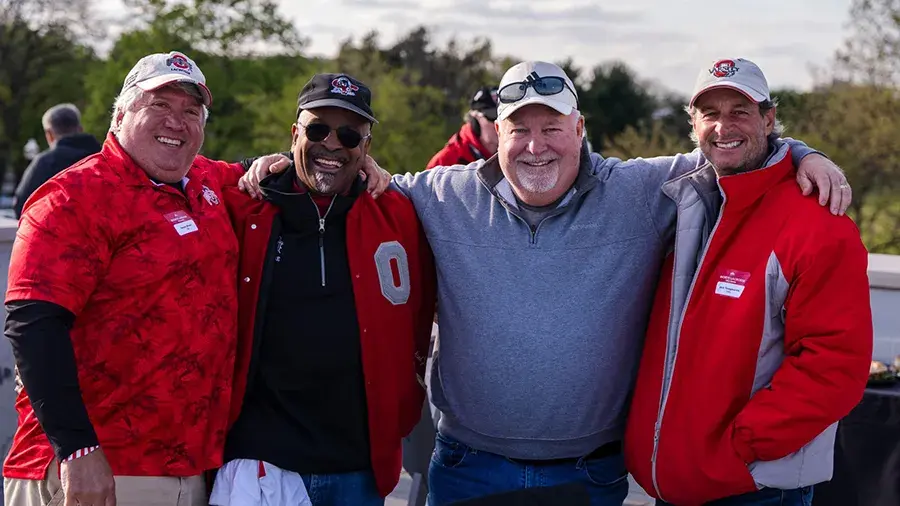 Four individuals in Ohio State gear posing for a photo with their arms around each other.