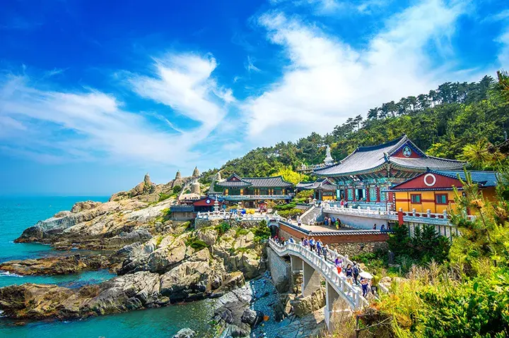 Cliffside temple overlooking the ocean, with visitors walking across a bridge toward the buildings