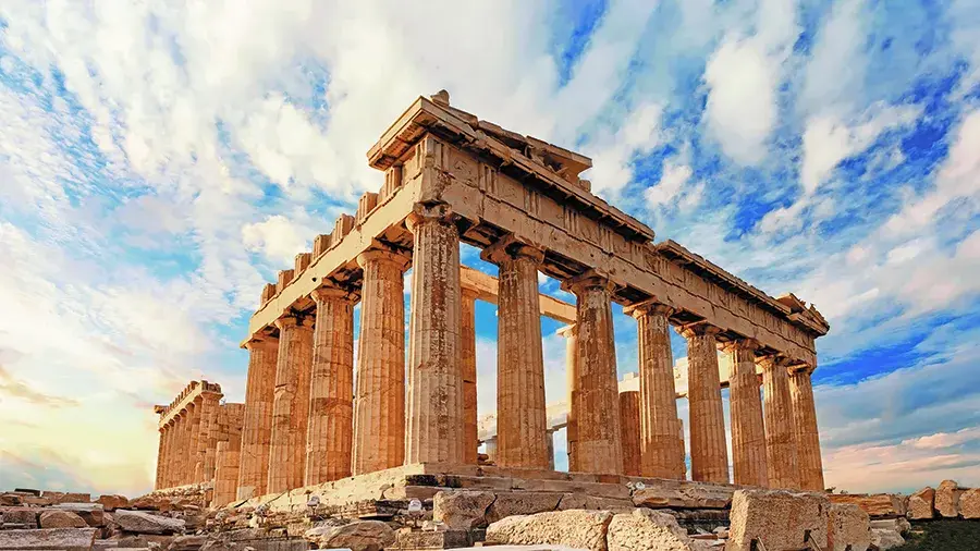 The Parthenon, an ancient Greek temple with tall stone columns, under a bright sky with scattered clouds.