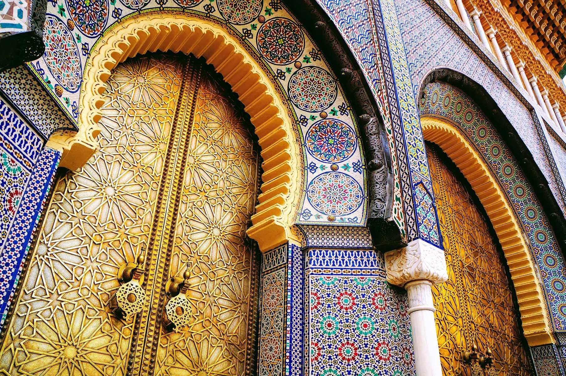 Ornate golden doors framed by colorful geometric tilework and arched carvings in traditional Moroccan architectural style