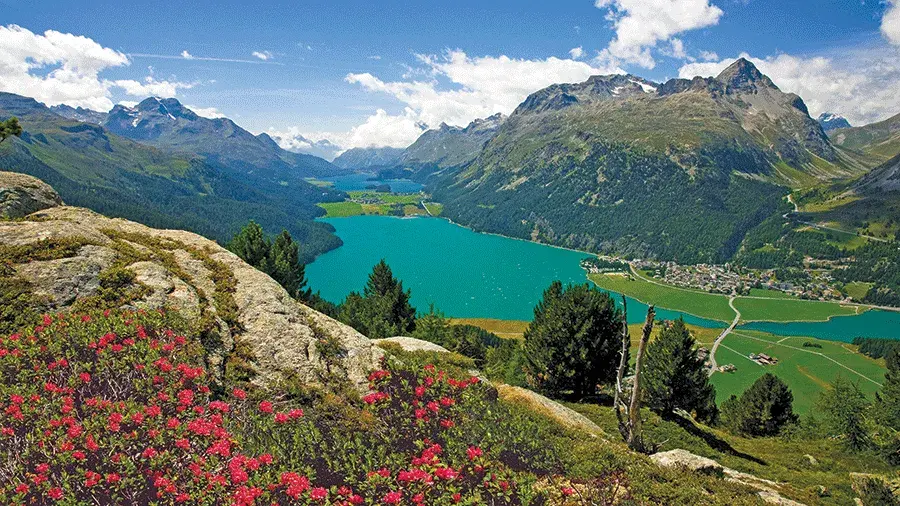 Swiss Alps surrounding a greenish blue lake with a bright blue sky in the background