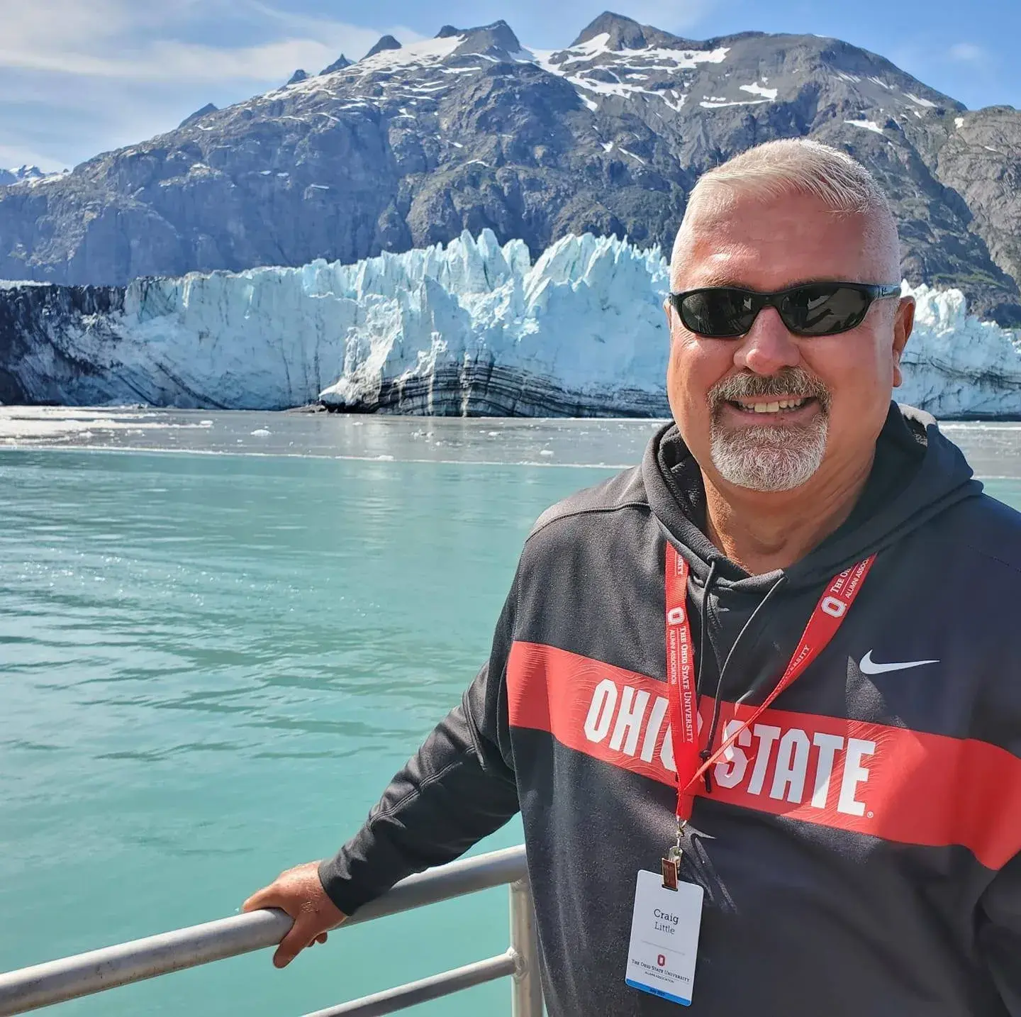 craig little, director of alumni engagement, smiling with his ohio state sweatshirt on standing infront of a mountain on an alumni tour