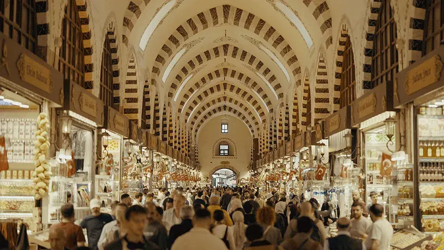 A crowded indoor market hall with a high arched ceiling, rows of small shops on both sides and many people walking through the central aisle.
