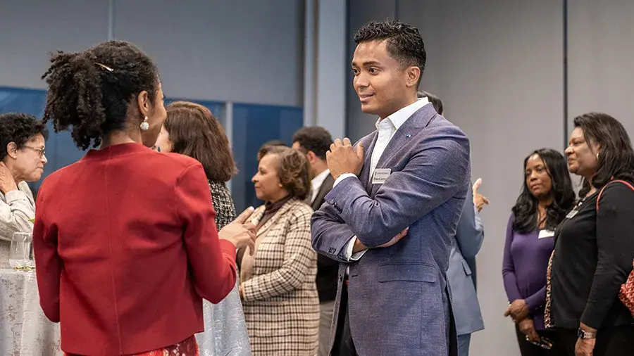 Group of adults wearing business attire and name badges standing and talking at an indoor networking event.