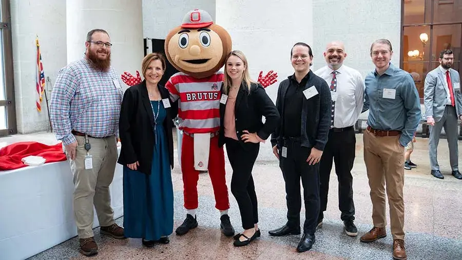 Group of adults wearing business attire and name badges posing for a photo with Brutus Buckeye.