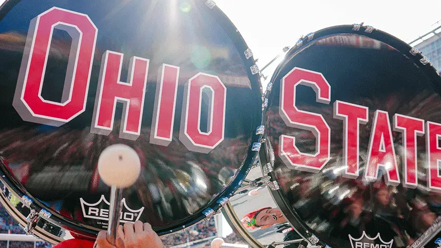 Two large bass drums with “Ohio State” printed in red and white are being played inside Ohio Stadium.