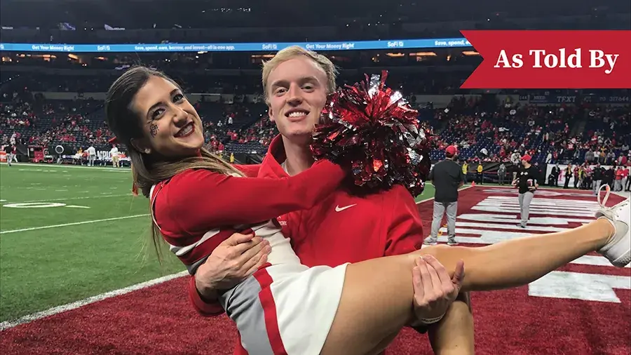 One Ohio State cheerleader holding another one in the endzone of a football stadium with a small red "As Told By" graphic in the top right corner.