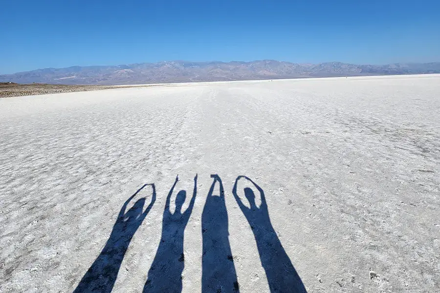 Four shadows on a bright salt flat form “O‑H‑I‑O,” with mountains in the distance under a clear blue sky.