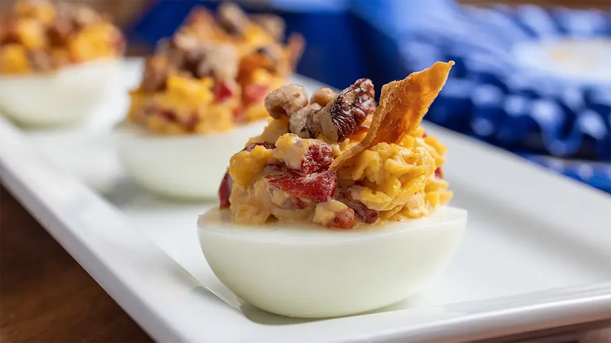 Deviled egg halves topped with a creamy filling, garnished with crispy bacon bits on a white rectangular plate.