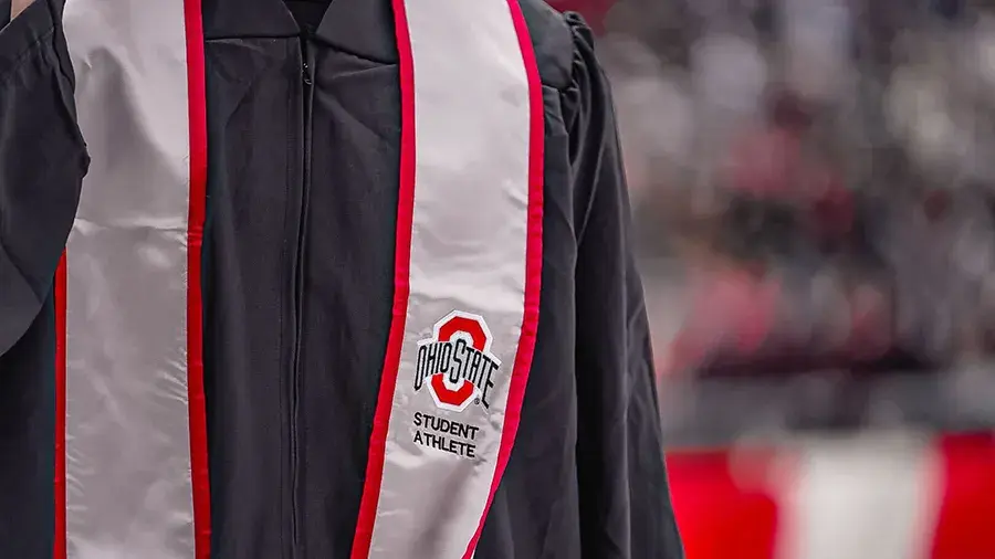 Close-up of a black graduation gown with a white stole trimmed in red. The stole displays the Ohio State logo and the words “Student Athlete.”