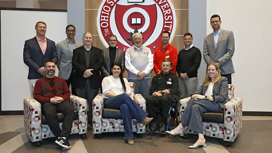 Group photo of 11 people posed beneath a large Ohio State University seal in a lobby.