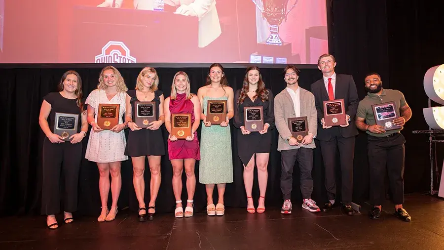 Scholarship recipients stand on stage holding award plaques during an Ohio State recognition event.