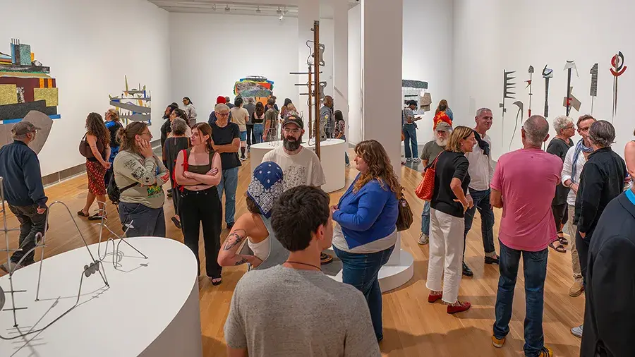 Visitors mingle and view artworks during a gallery opening in a large, bright museum space.
