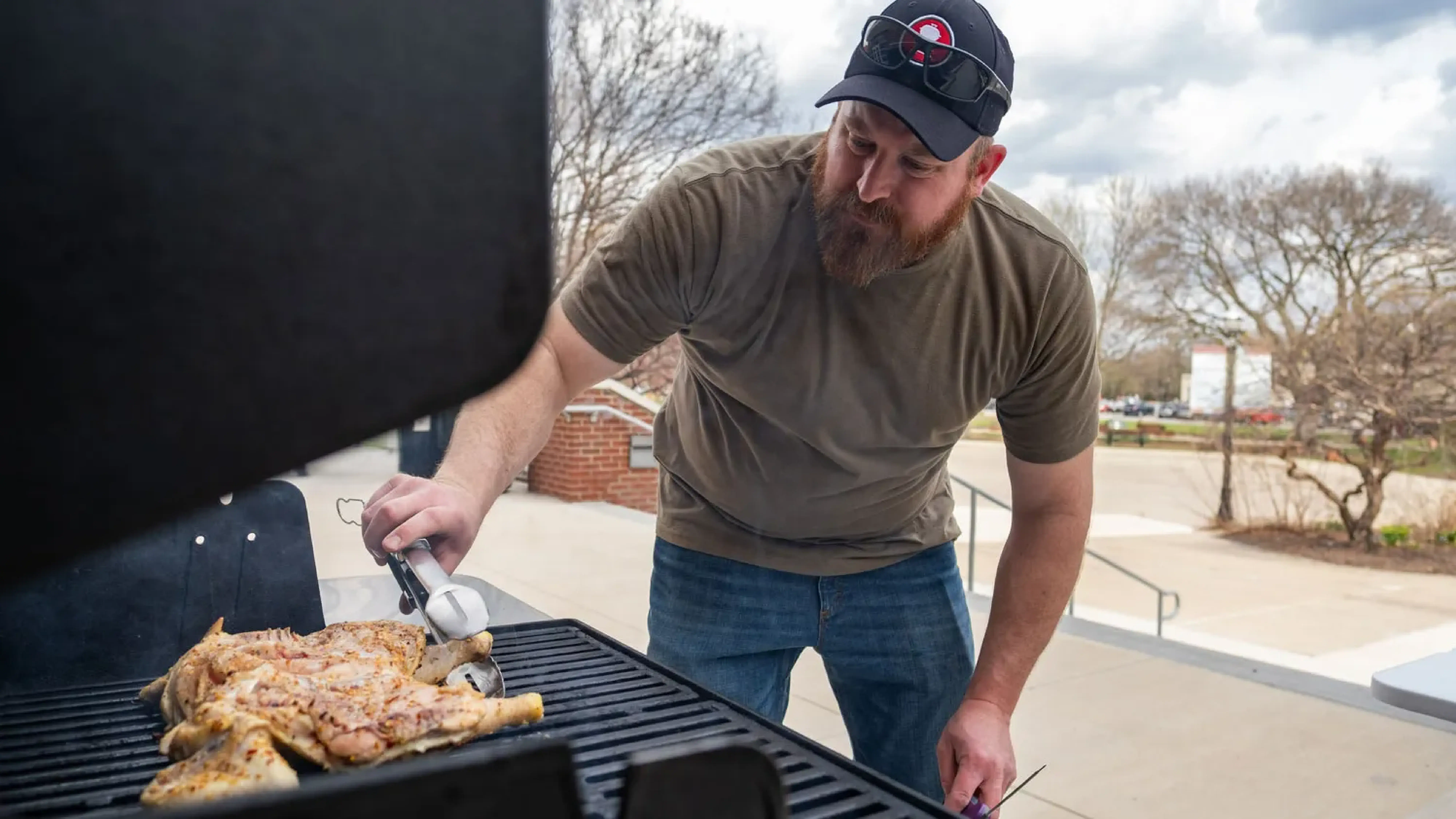 Person using tongs to cook chicken on an outdoor grill.