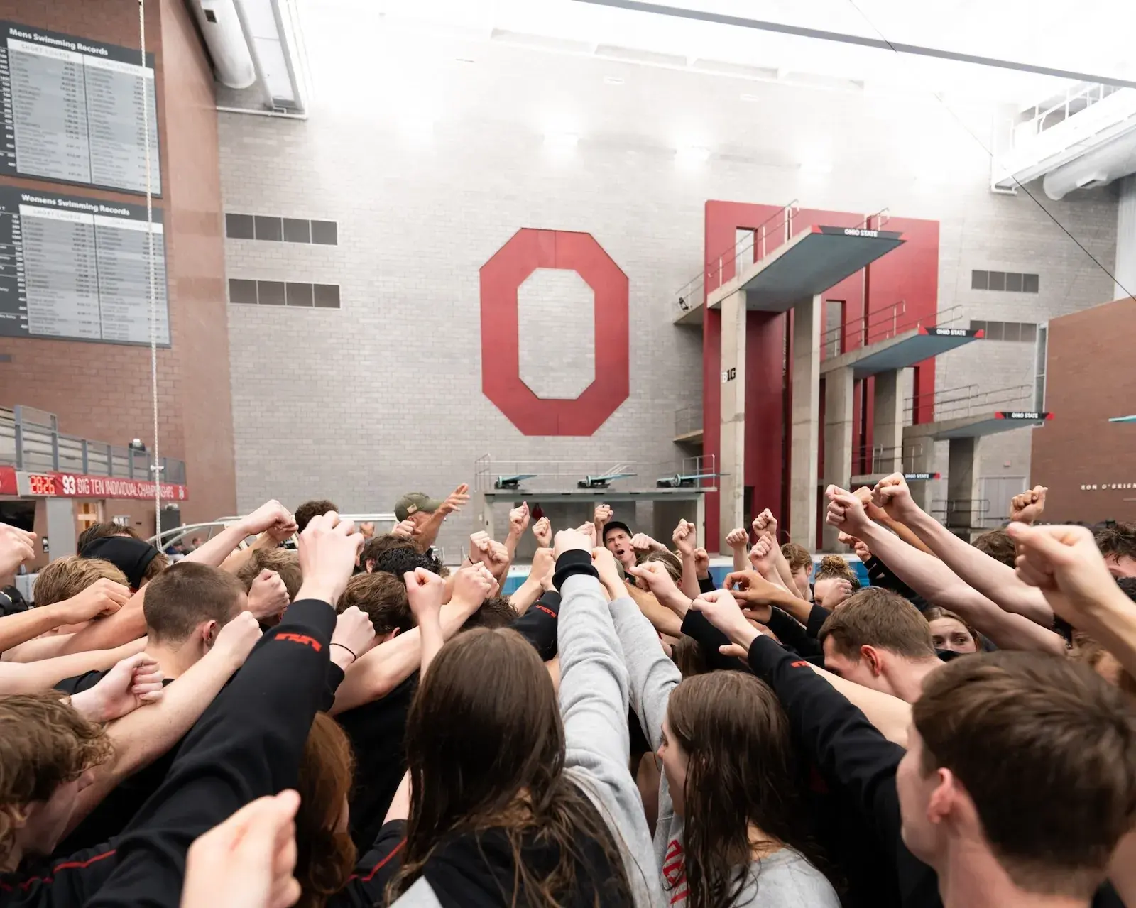 Group of varsity O swim students holding their hands up in front of an Ohio State O sign 