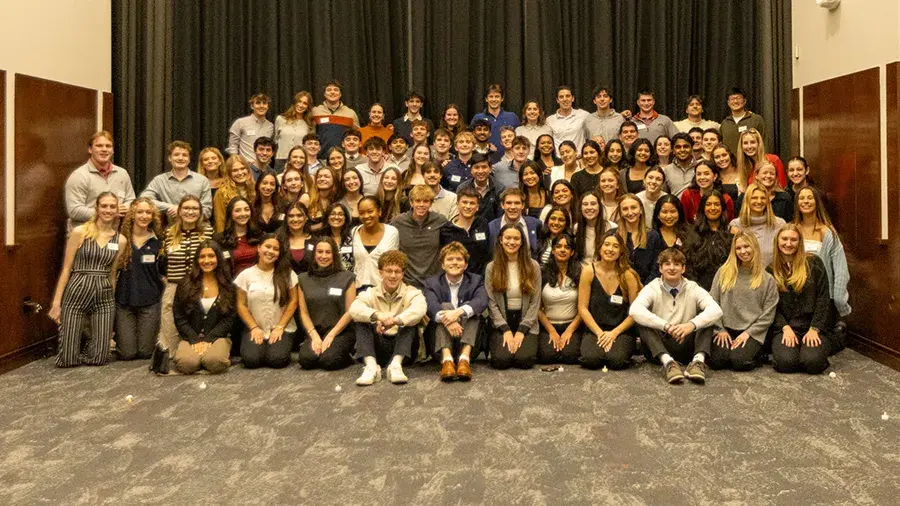 A large group of people pose together for a group photo in an indoor meeting or event space.