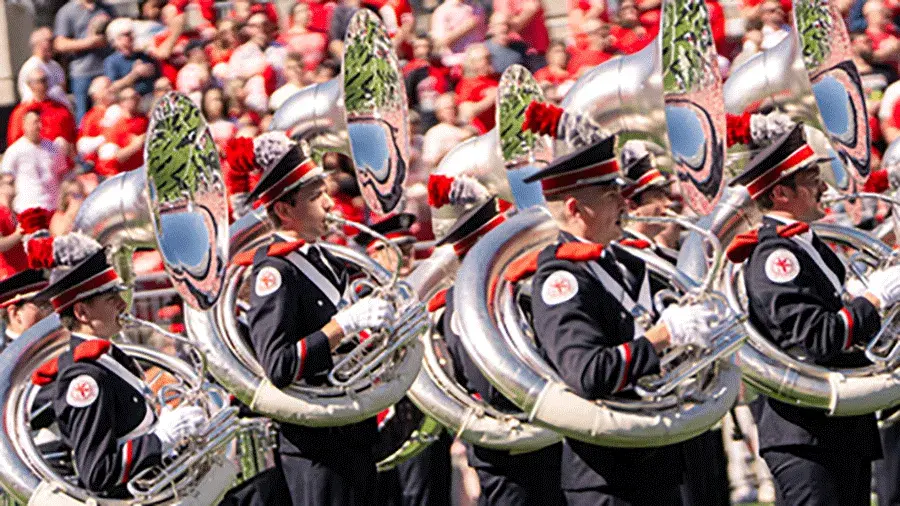 The Ohio State University Marching band members, performing during a football game, with a large crowd in the background.