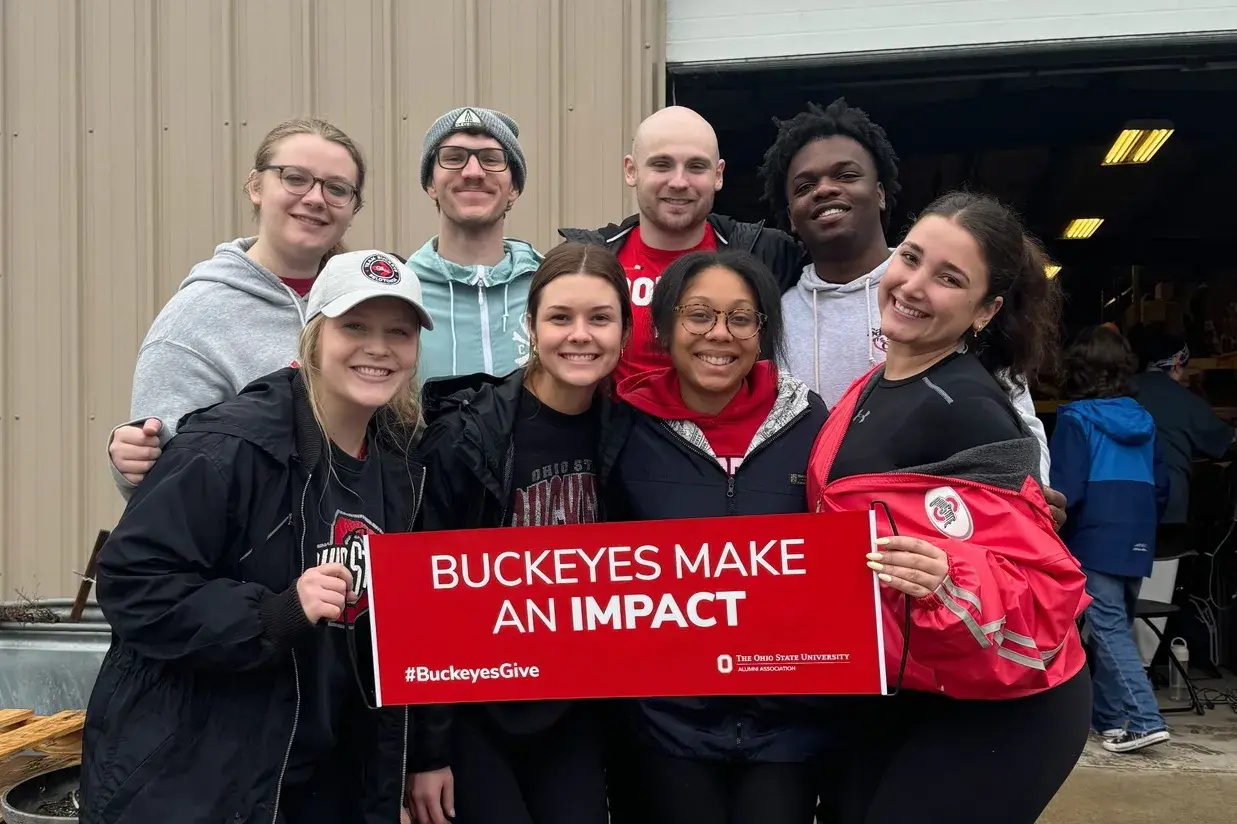 eight buckeye volunteers holding a scarlet sign that reads 'buckeyes make an impact'