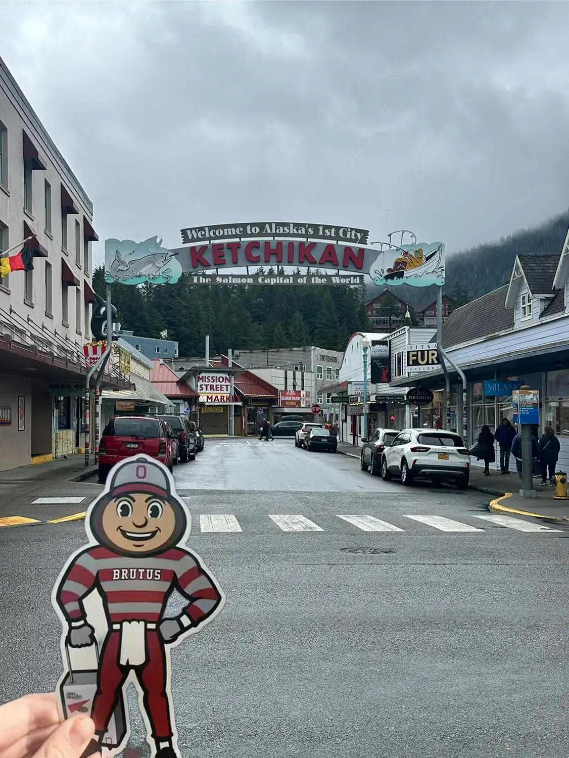 Brutus in front of a small town and a sign that says: Welcome to Alaska's 1st City - Ketchickan"