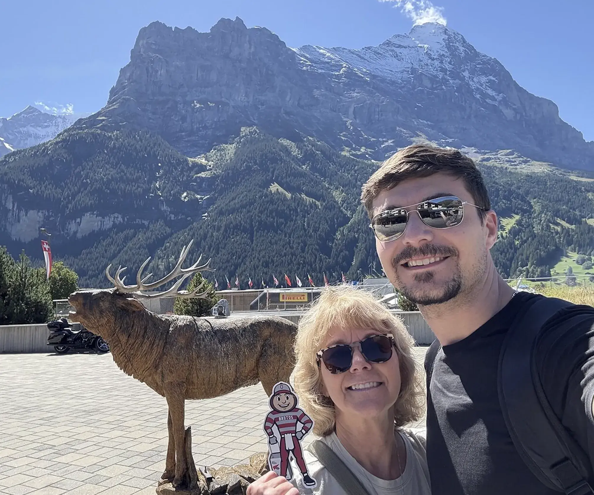 Brutus with a man and woman in front of a moose statue with the mountains in the background.
