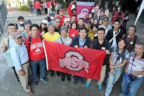 alumni standing and smiling while holding a ohio state flag