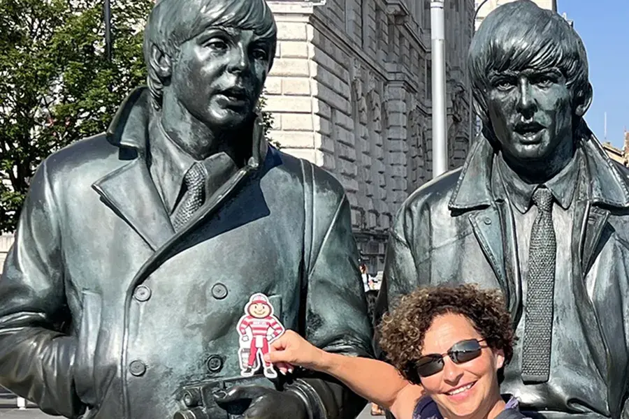 Brutus Buckeye is held up beside the Beatles statue on Liverpool’s waterfront in England, with a visitor in sunglasses posing in front of the bronze figures.
